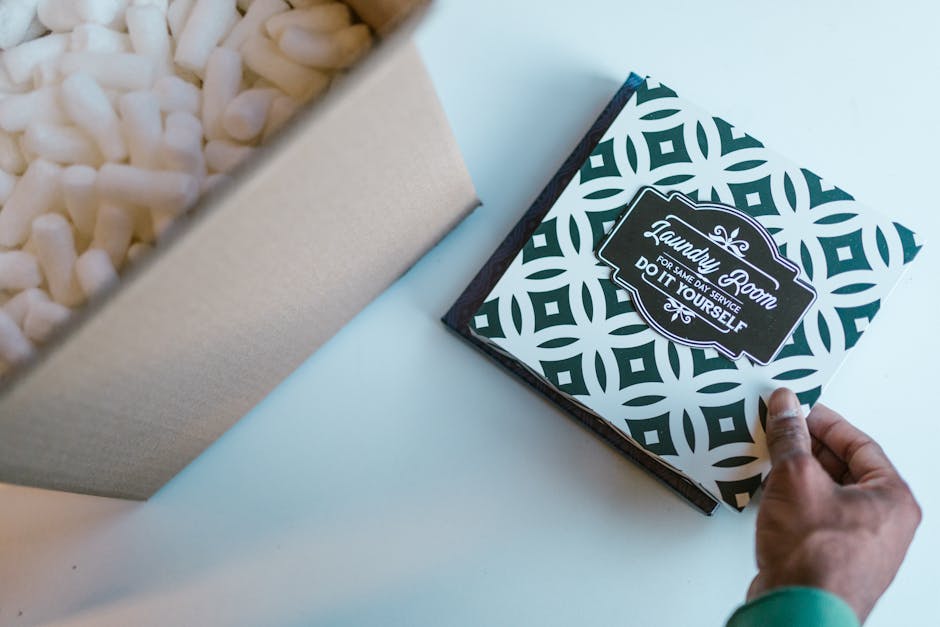 A person’s hand is seen opening a decorative box with a black and white geometric pattern, revealing a label that reads 'Laundry Room for same day service do it yourself.' Next to the box is a beige