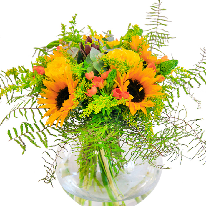 This abundant bouquet, meticulously arranged near Bellingham's bustling high street, evokes the enduring joy of the area's sunniest days. Majestic sunflowers-with rich yellow petals radiating like the sun above Beckenham Place Park-command your attention, their textured centers a grounding force within the arrangement. Clusters of buttery yellow garden roses unwind in harmonious spirals, their velvety softness punctuated by shiny red Hypericum berries that glisten as though kissed by morning dew. Threads of lush greenery-airy ferns, light green filler, and the subtle sheen of eucalyptus-spill outward, softening the arrangement's lively yellows and adding dimension reminiscent of riverside walks. The clear, rounded vase reveals every stem's path, cradling the bouquet as sunlight dances across the glass and water below. Up close, you can almost sense the crisp snap of fresh foliage and the gently sweet floral scent rising on the breeze. Perfect for celebrating milestones in Bellingham-from family birthdays to cherished anniversaries-this bouquet embodies happiness, artistry, and the careful craftsmanship of a dedicated local florist, ready to brighten any home or occasion.